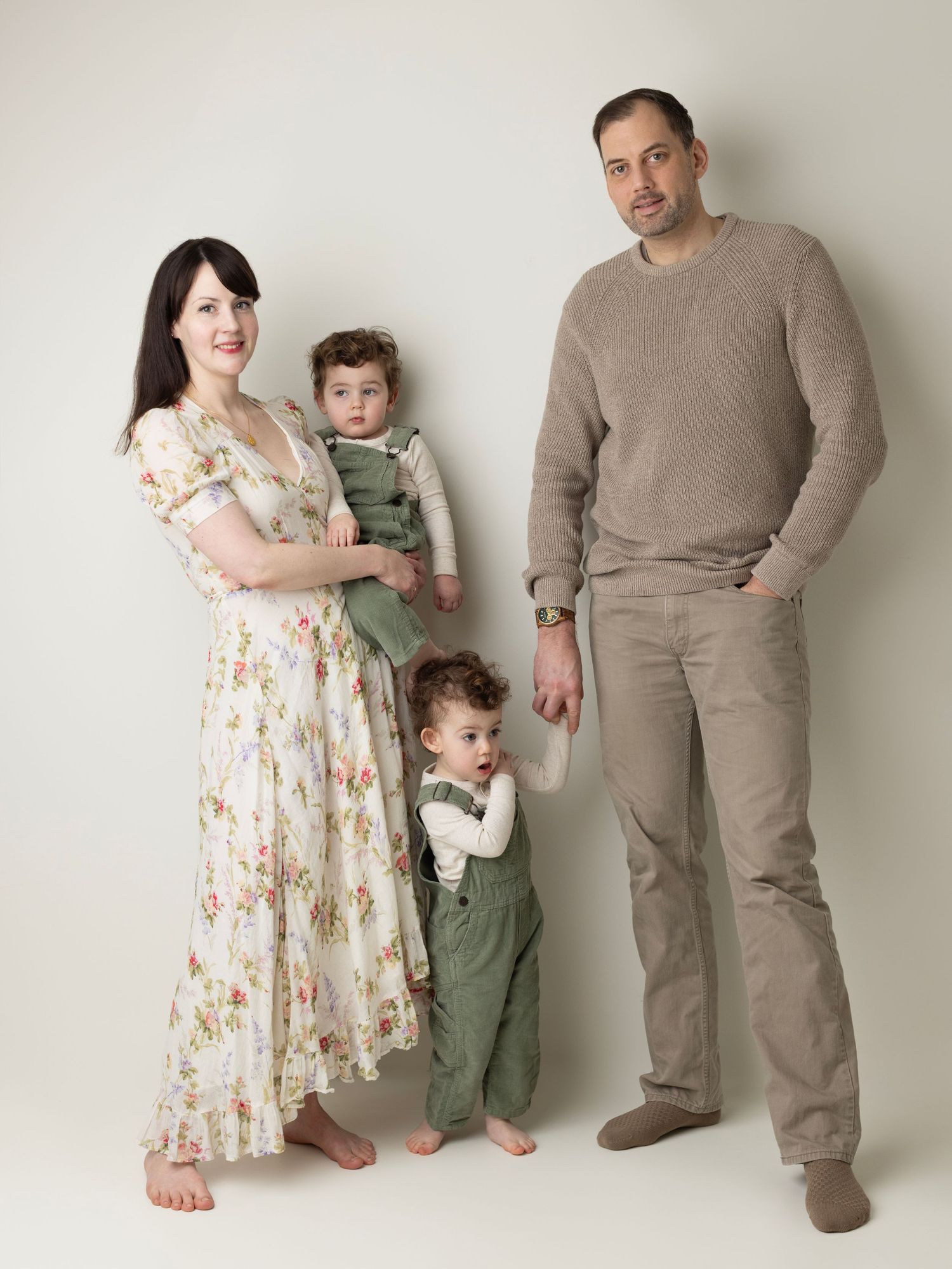 Family wearing coordinated beige and green outfits pose together against white backdrop in studio setting.