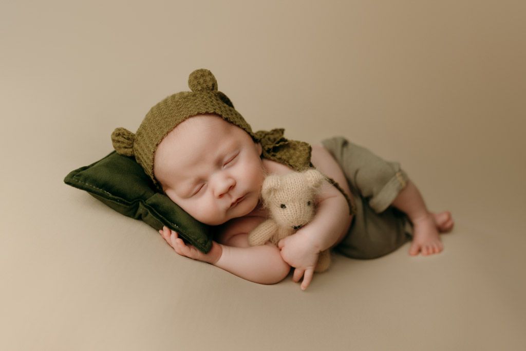 A sleeping newborn baby in neutral tones curls up with a small plush toy on a soft beige backdrop carefully curated by studio in victoria bc
