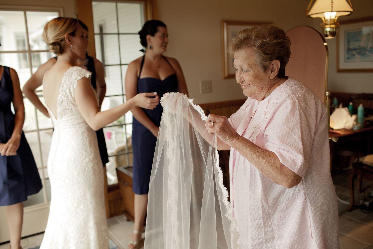 Wedding preparation scene showing bridesmaids in a sunlit room helping with final touches.