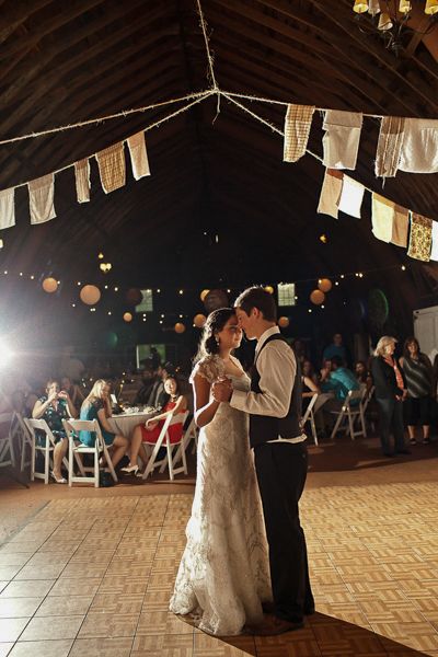 Wedding reception first dance in rustic barn venue with string lights and lanterns.
