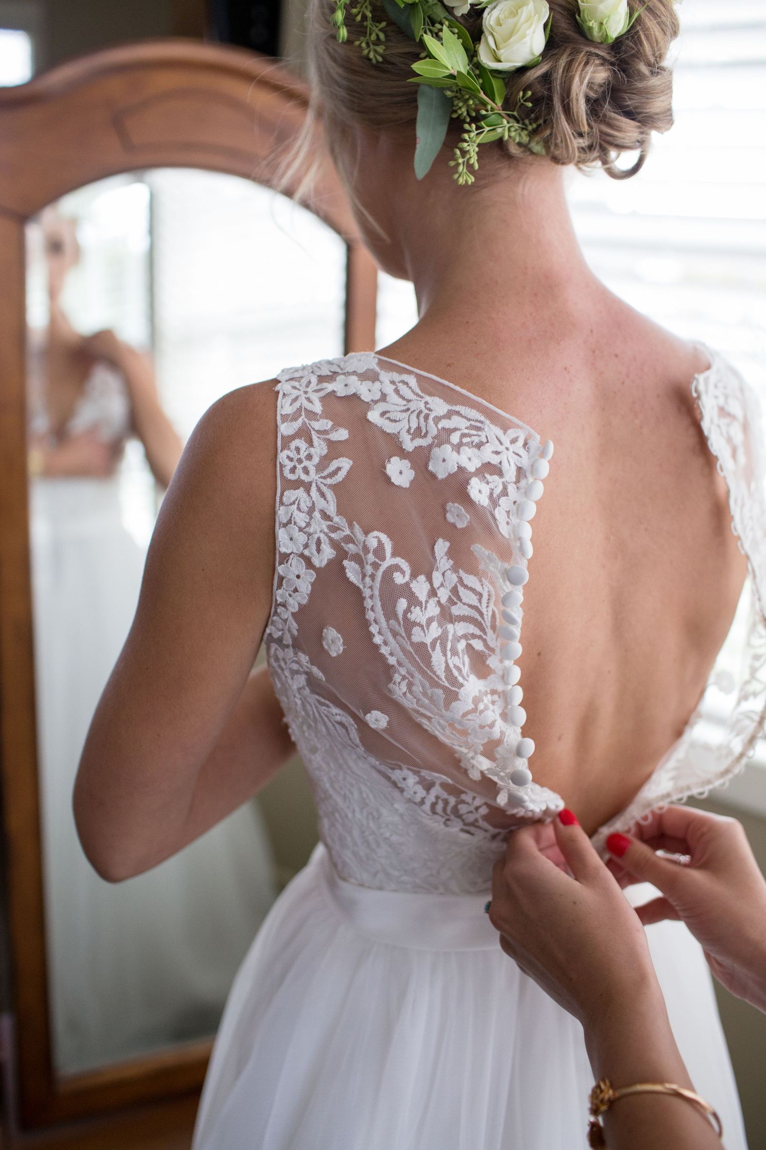 Close-up details of delicate white lace on the back of a wedding dress being fastened.