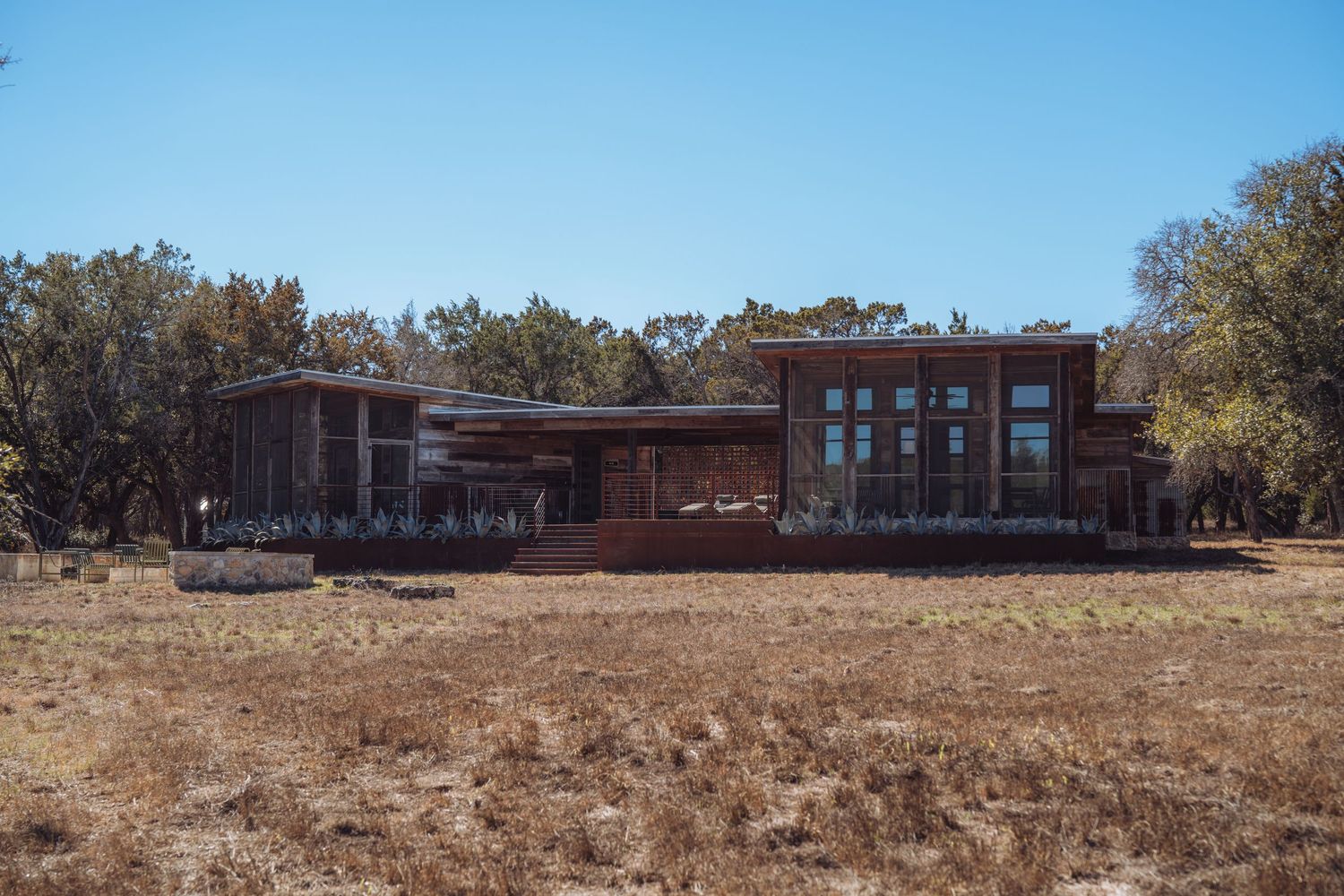 A panoramic view of a rustic desert lodge with wooden architecture nestled among trees against a bright blue sky.