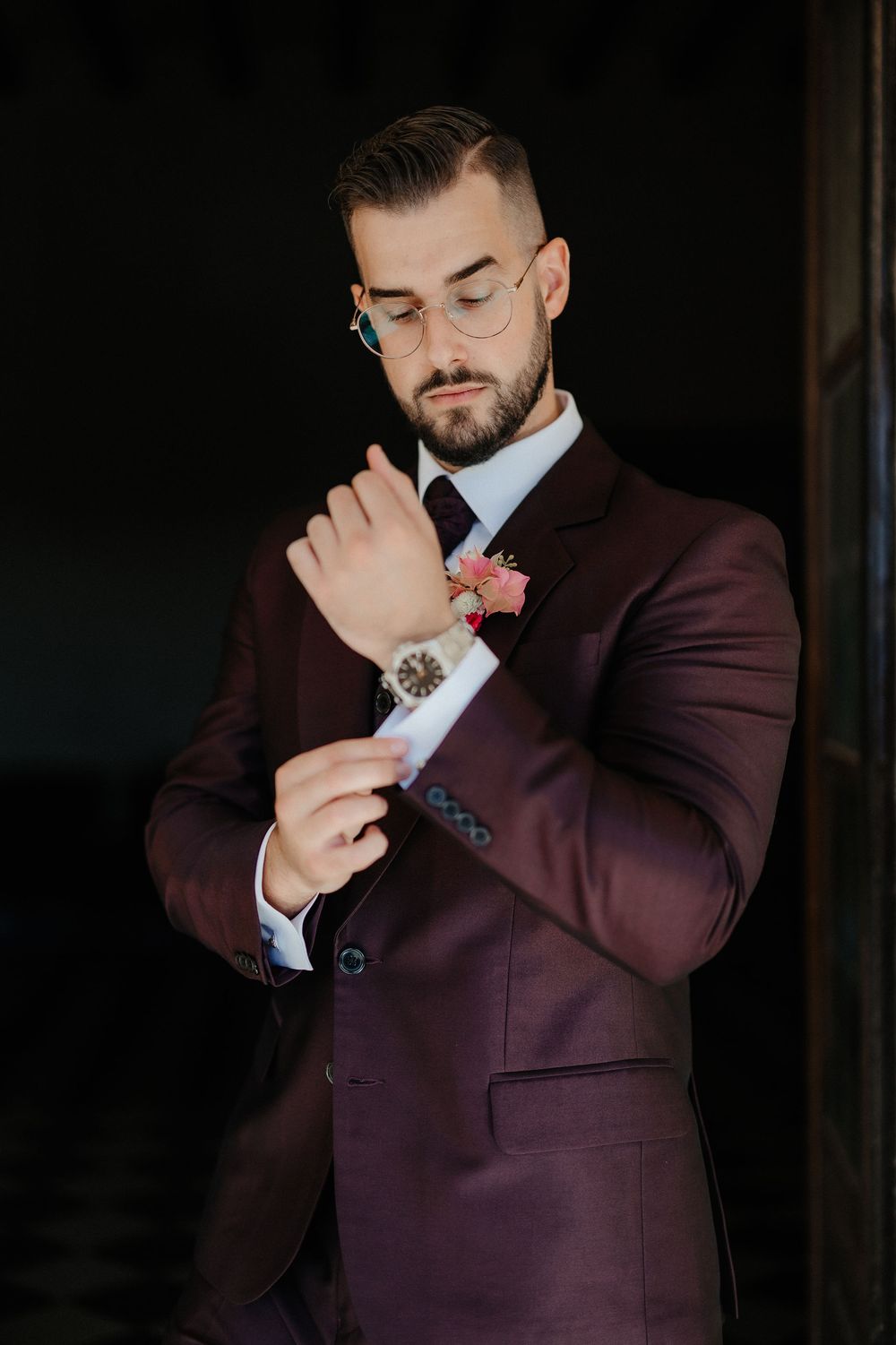 A person in a burgundy suit and light blue shirt poses in a series of dramatic shots against a dark background.