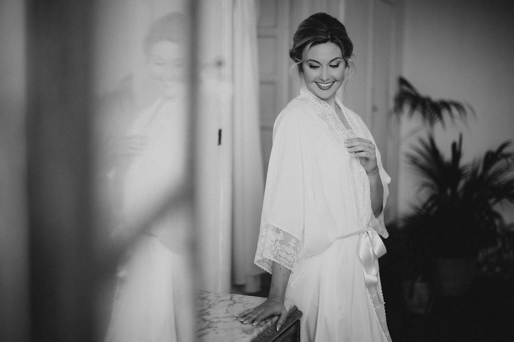 A person in a white dress smiles while getting ready in a softly lit room with vignette lighting effects.