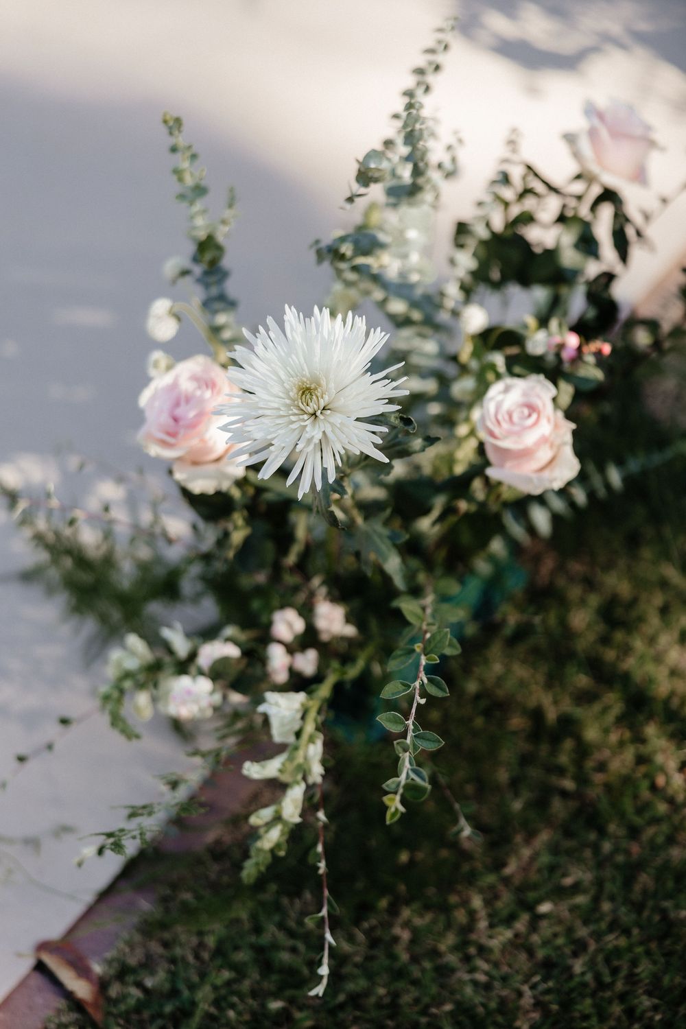 A delicate arrangement of pink roses and white spider mums with trailing greenery against a cloudy sky.