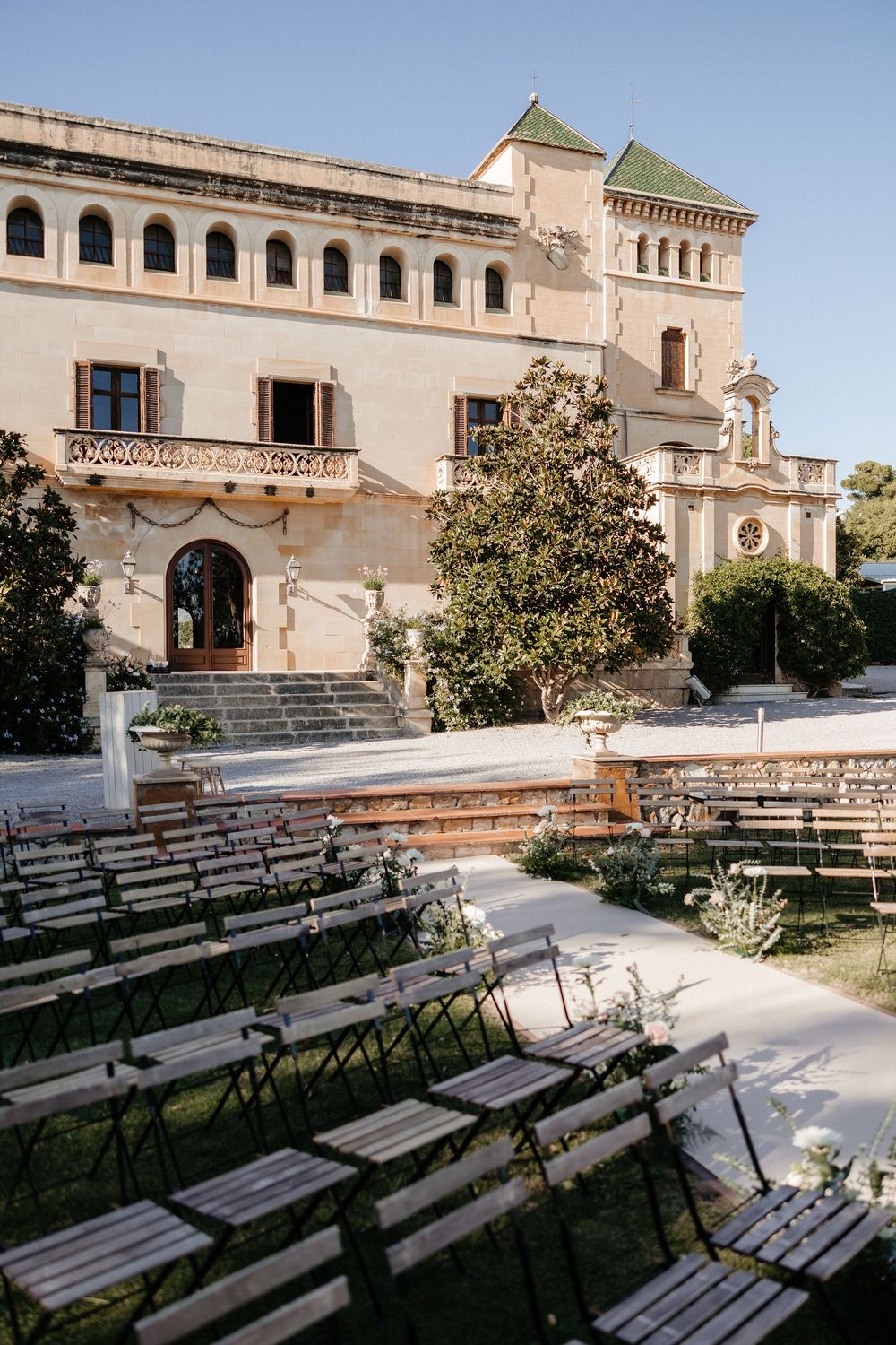 Rows of empty wooden benches arranged in an amphitheater style seating area facing a historic Mediterranean-style building.
