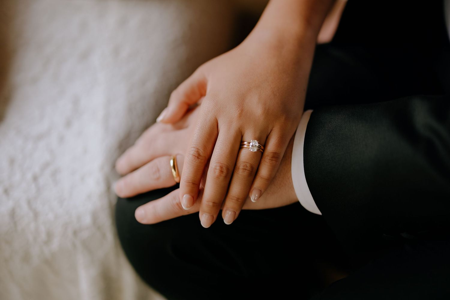 Close-up shot of hands wearing a diamond engagement ring against a white textured background.