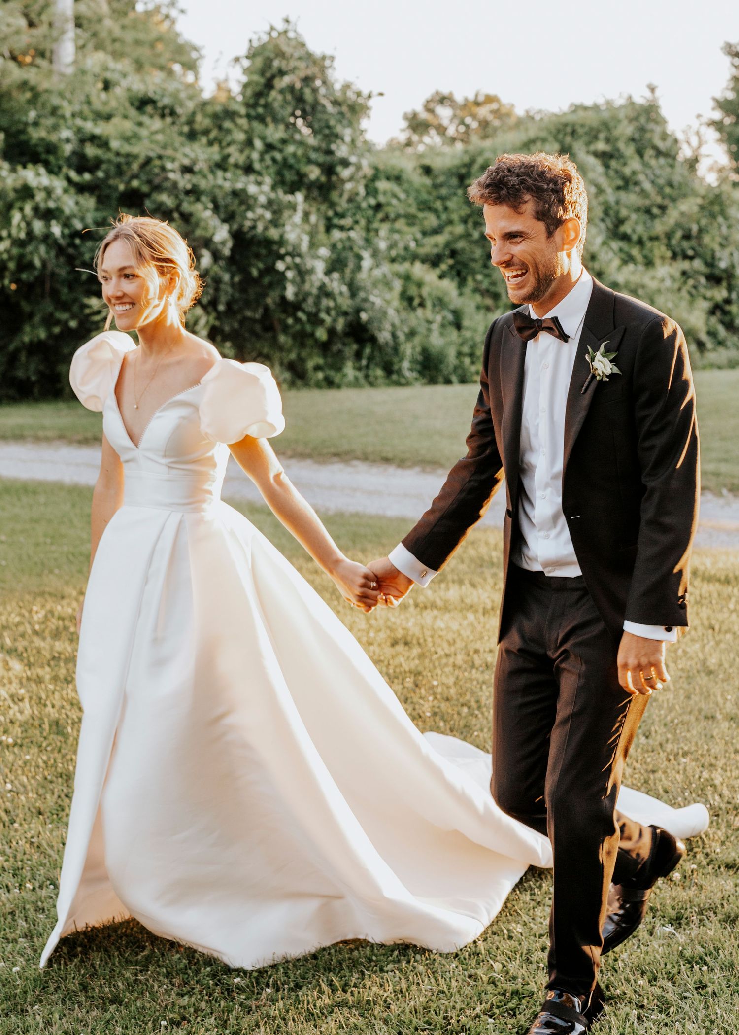 Elegant wedding couple walking through a sunny field in formal attire.