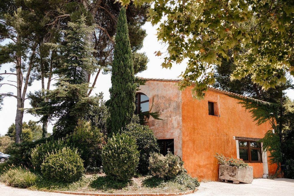 Mediterranean-style terracotta villa with lush greenery and trees surrounding the entrance.