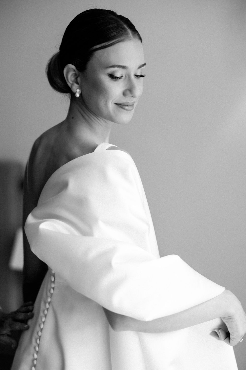 Black and white portrait of someone in a white wedding dress with elegant hair styling and pearl earrings.