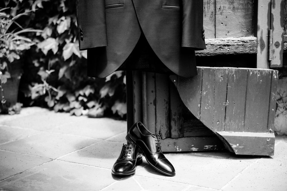 Close-up black and white photo of formal dress shoes and suit pants standing on wooden steps.