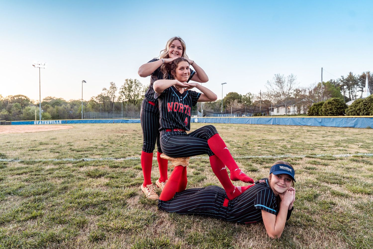 A person in red pants and black top performs a series of stretching exercises on a grassy field at sunset.