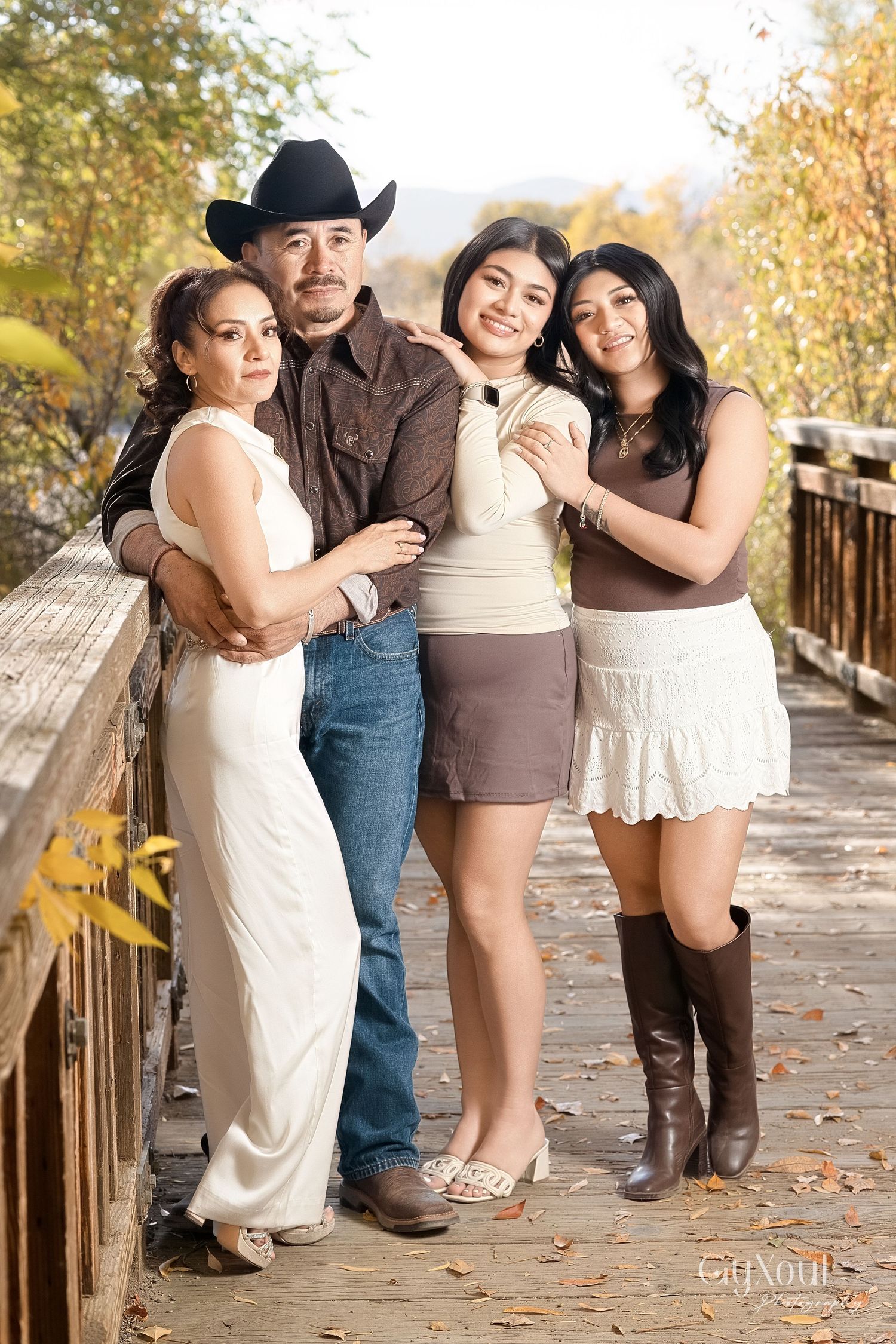 A group poses together on a wooden bridge during autumn with fall foliage in the background.
