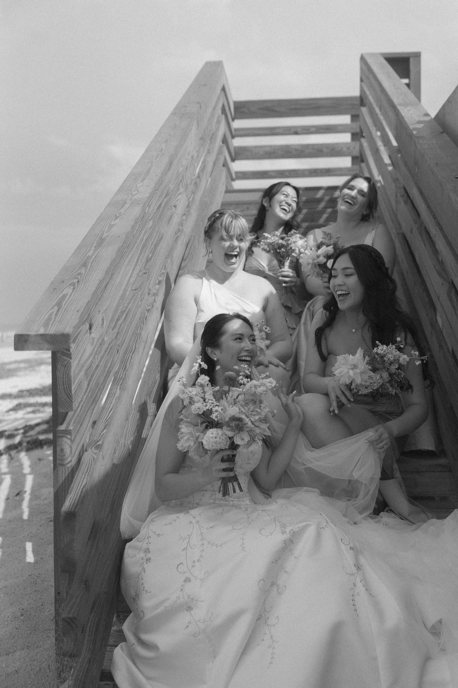 A group of groomsmen in white shirts and dark pants share a candid laughing moment together on a bench outdoors.