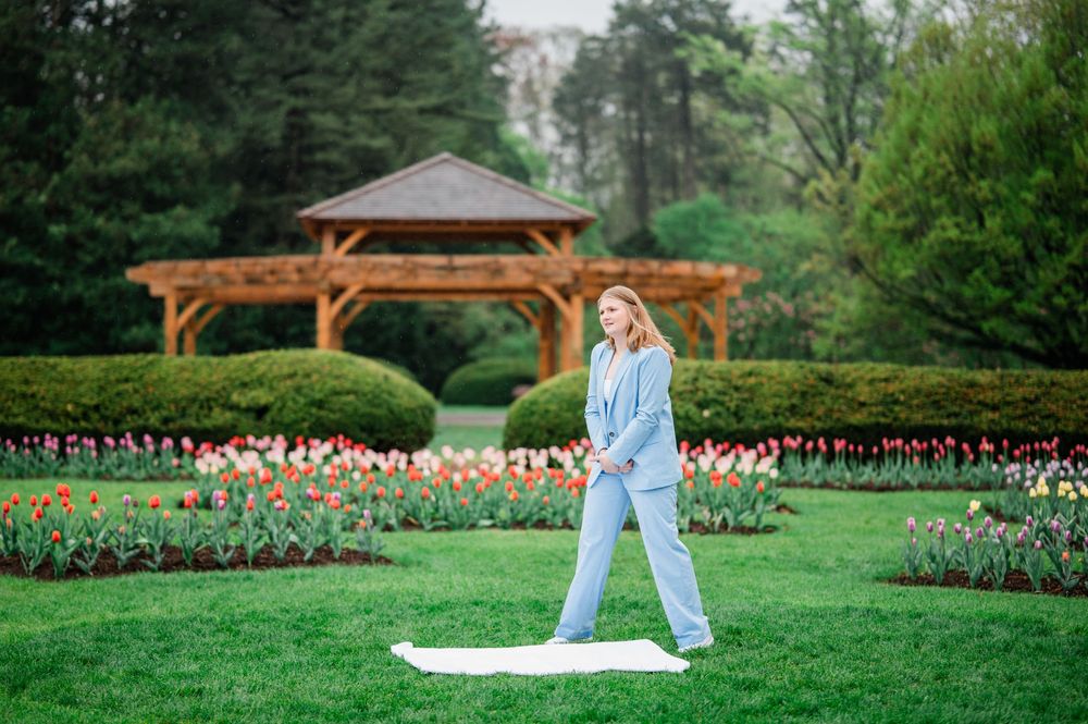 A garden scene with a wooden gazebo and colorful tulip beds as someone stands on a white cloth on the lawn.