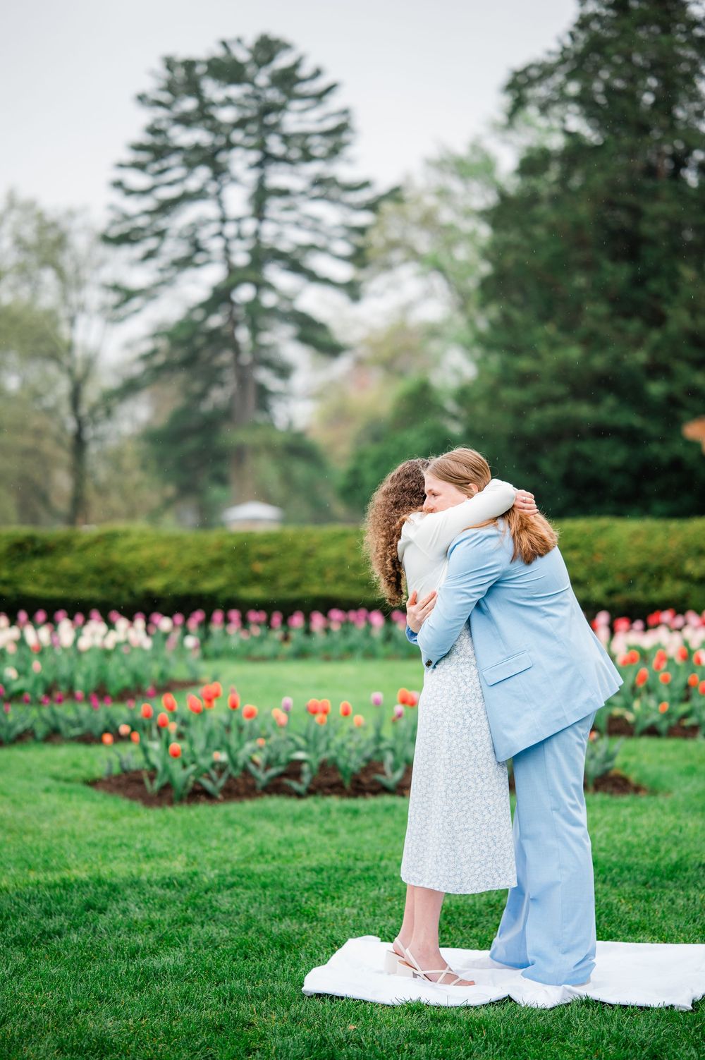 A couple embraces in a garden filled with vibrant tulips on a spring day.