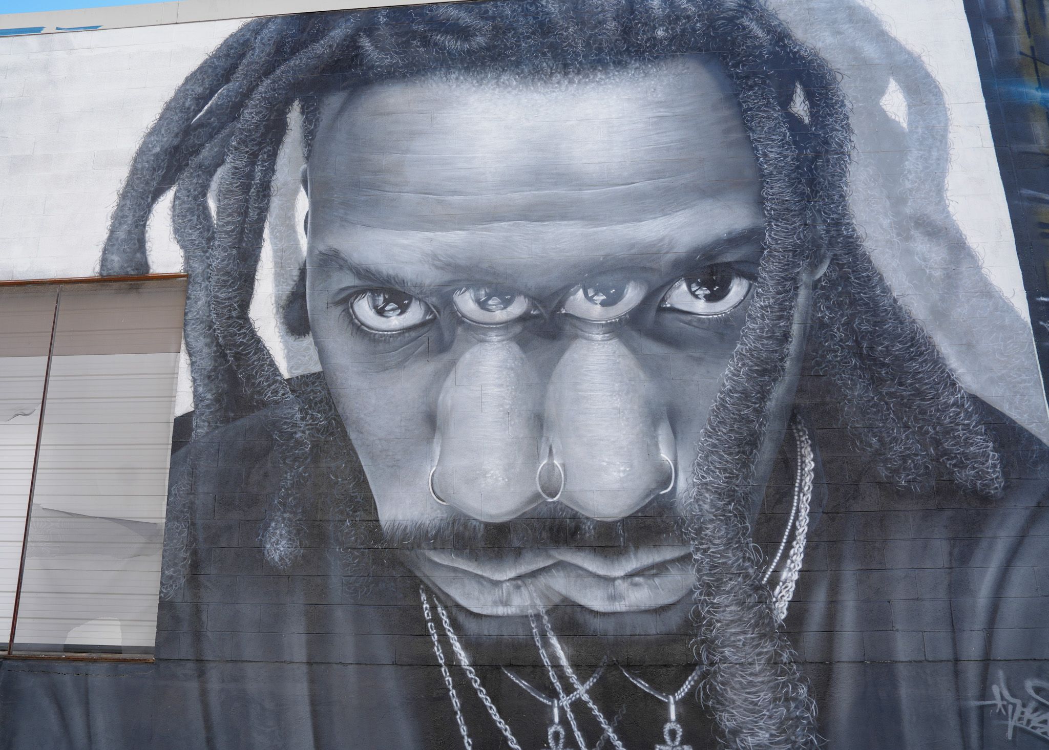 Large black and white mural of a man with dreadlocks and nose rings on building exterior.