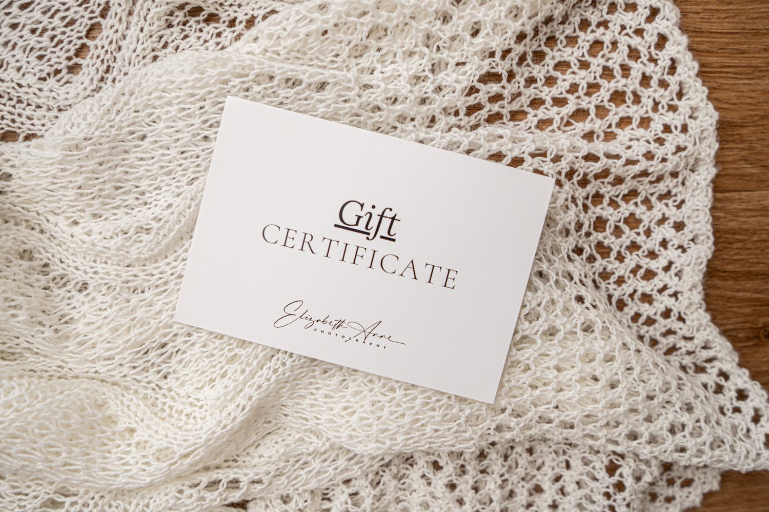 White gift certificate card placed on delicate lace fabric with wooden surface in background.