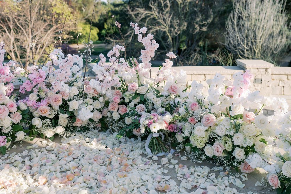 A romantic wedding arch decorated with pink and white flowers stands elegantly against a stone wall backdrop.