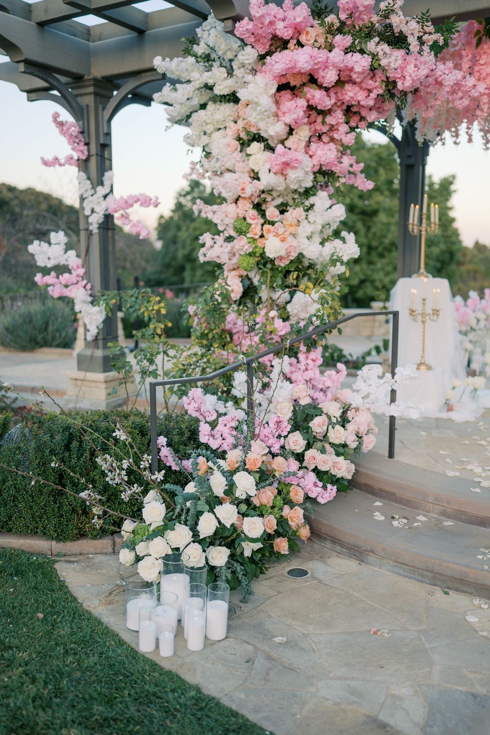 Elegant wedding ceremony setup with pink cherry blossoms and white roses decorating a stone gazebo path.