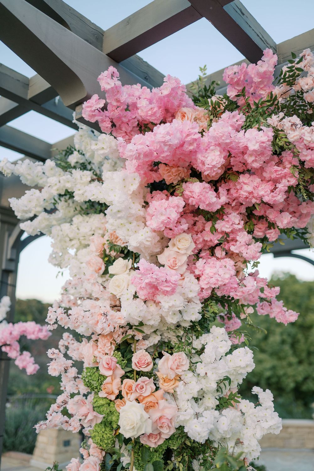 Elegant floral arch with cascading pink and white roses and peonies adorns an outdoor wedding ceremony space.