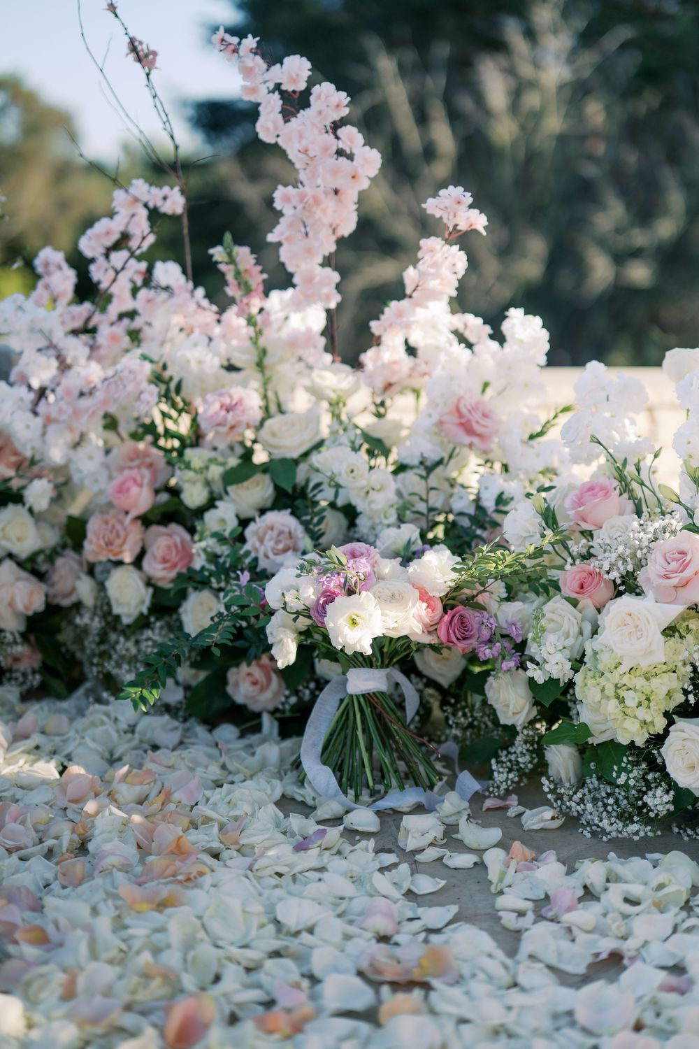 Elegant floral arrangement with pink and white roses, cherry blossoms and baby's breath scattered on petal-covered ground.