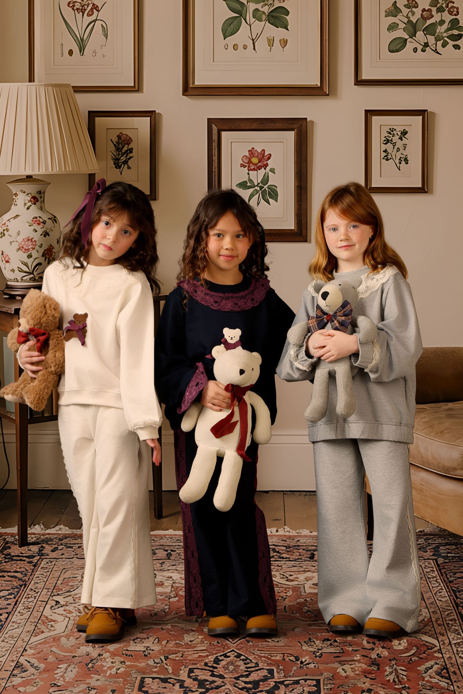 Children stand in a line against a wall with botanical prints, each holding teddy bears and stuffed animals.