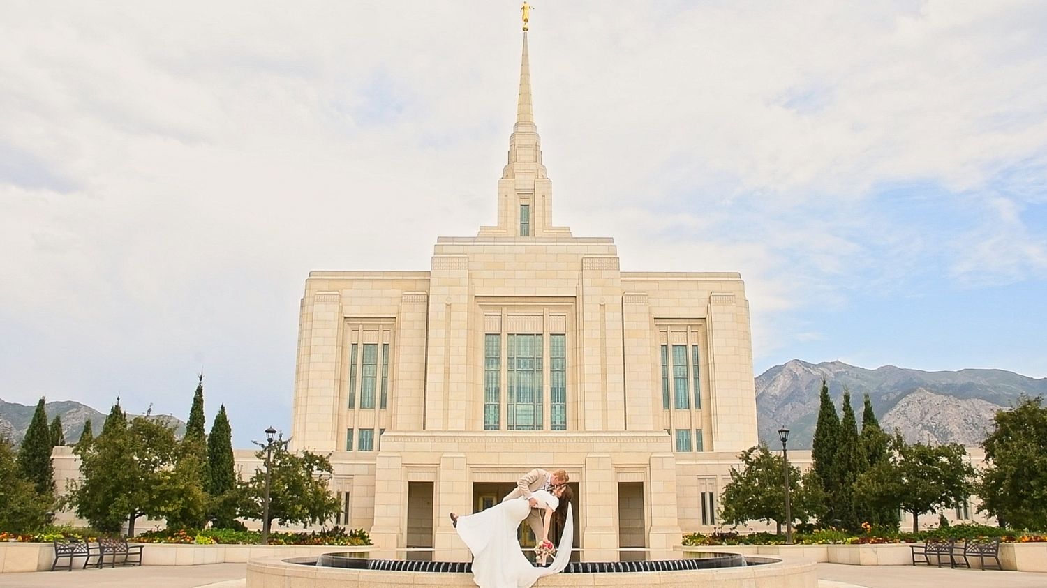 White temple building stands majestically against a Utah mountain backdrop and blue sky.