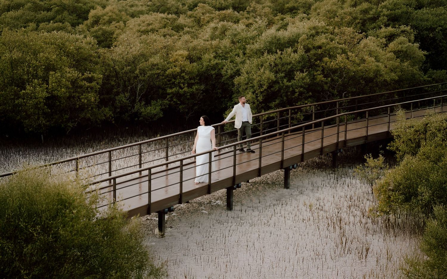 ride and groom walking on wooden bridge surrounded by lush greenery during outdoor wedding session in Abu Dhabi