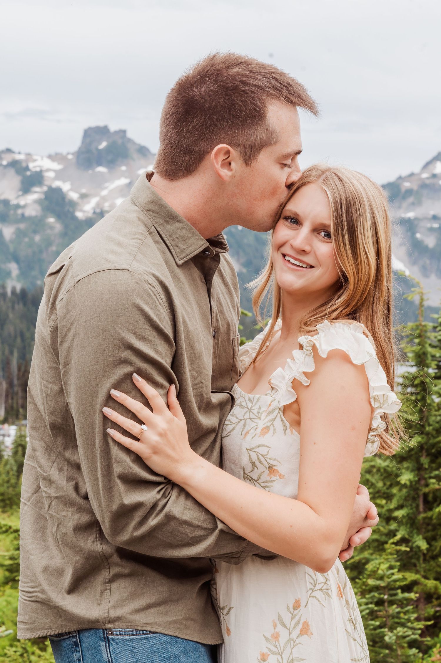 A couple embraces in front of snow-capped mountain peaks during an outdoor photo session in nature.