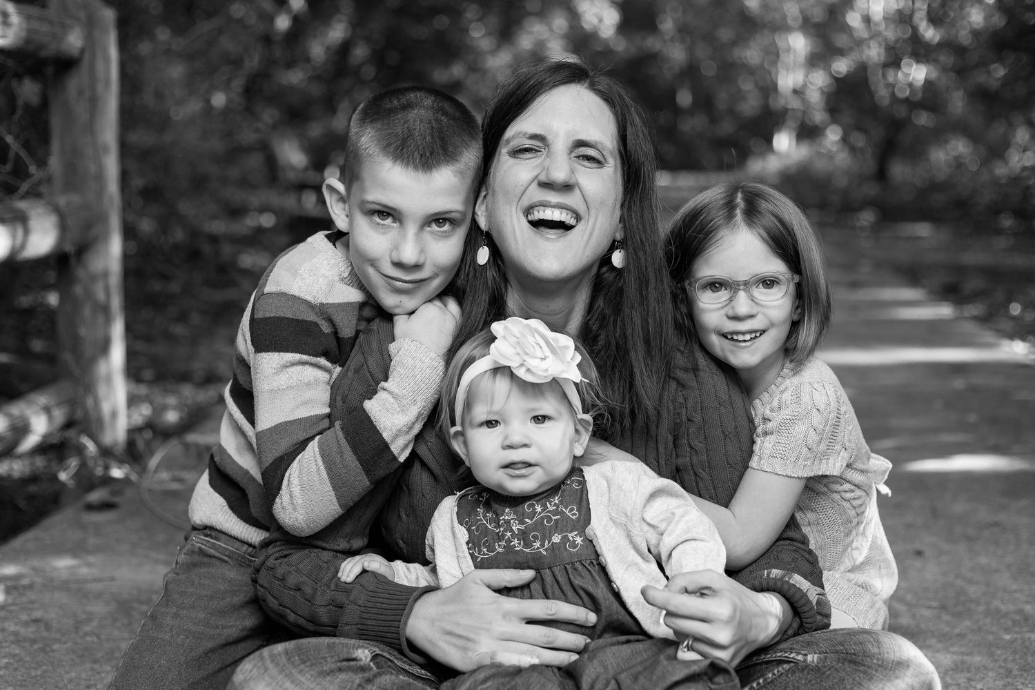 A black and white photo series showing a family sitting together and laughing during an outdoor portrait session.