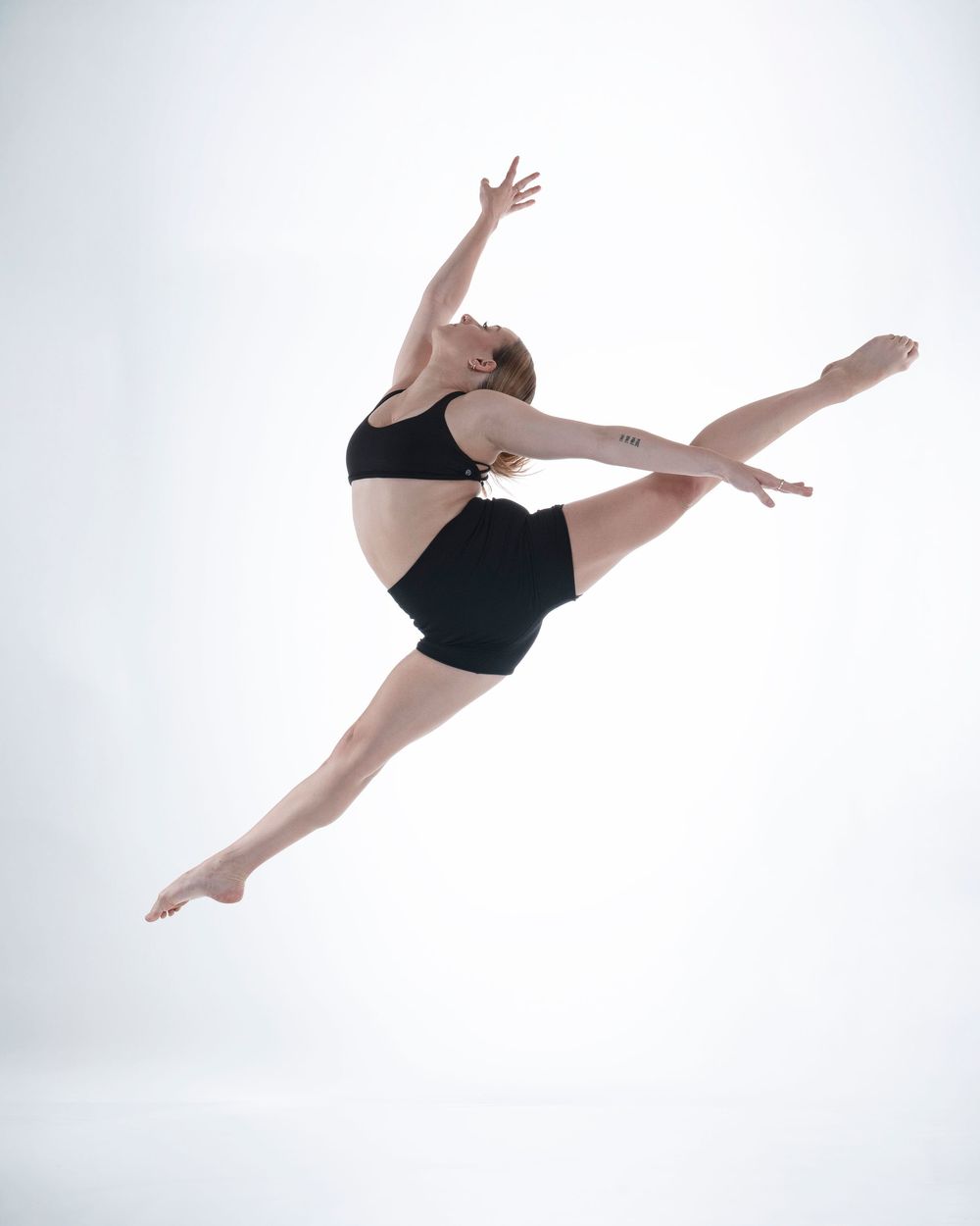 Graceful dancer in black performs a dynamic split leap against a white background.
