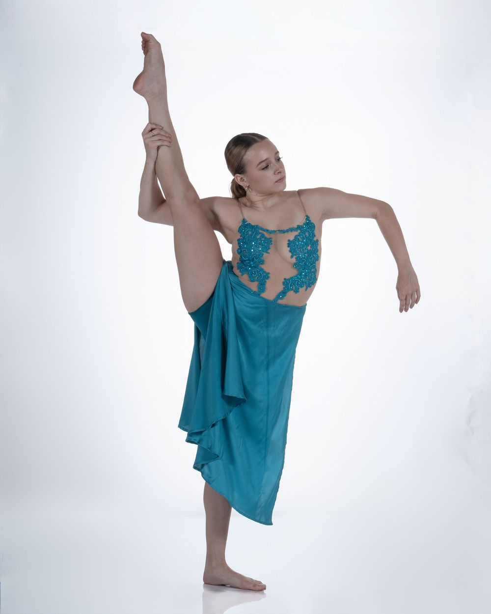 A dancer in a flowing turquoise dress performs a graceful contemporary dance sequence against a white backdrop.