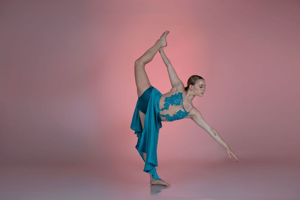Graceful dancer in flowing turquoise dress performs dynamic movement sequence against pink backdrop.