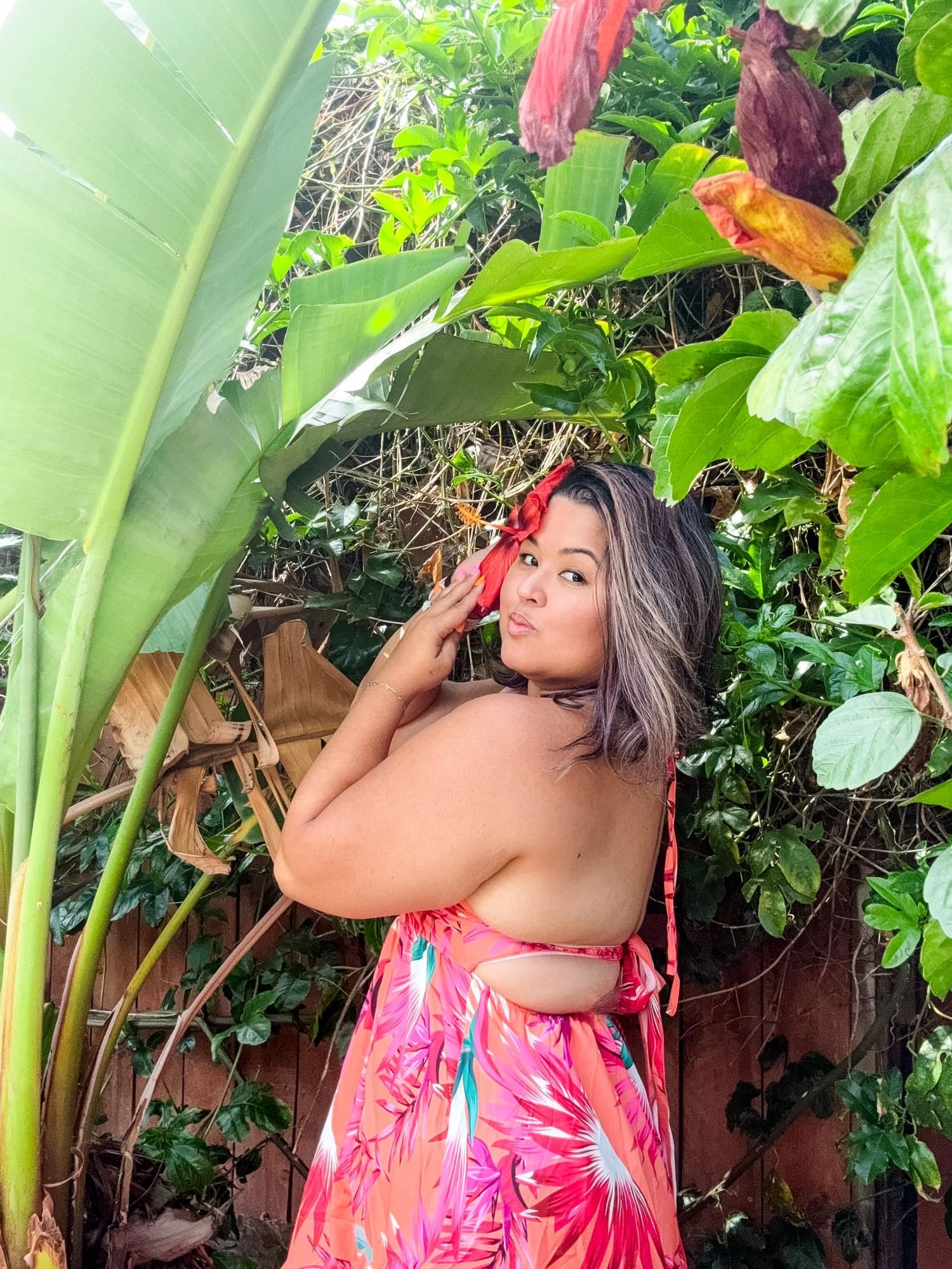 Tropical garden photoshoot featuring a pink floral dress against lush green foliage.
