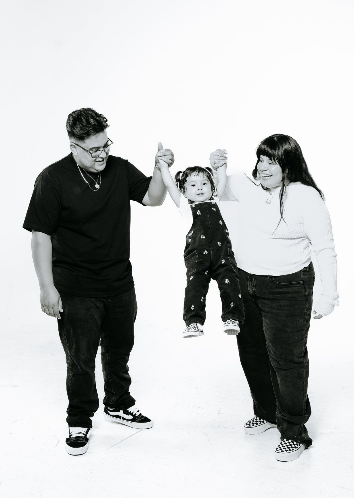 Black and white studio portrait of family having fun while lifting small child.