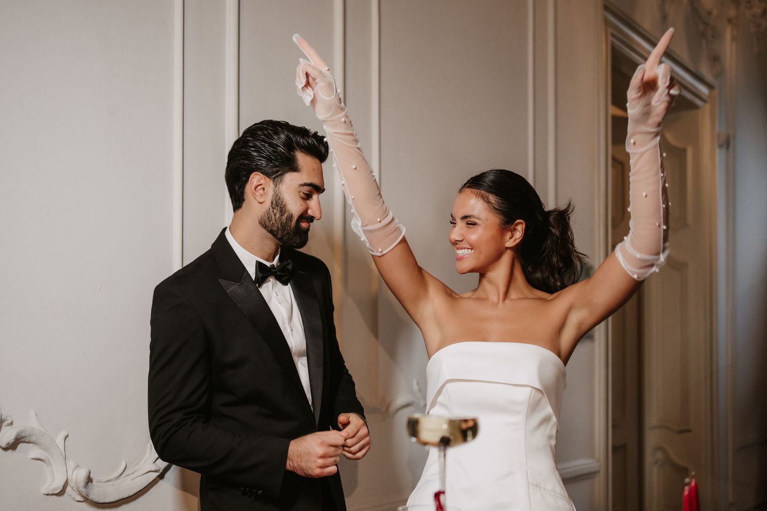 Celebratory moment with raised arms in elegant wedding attire.