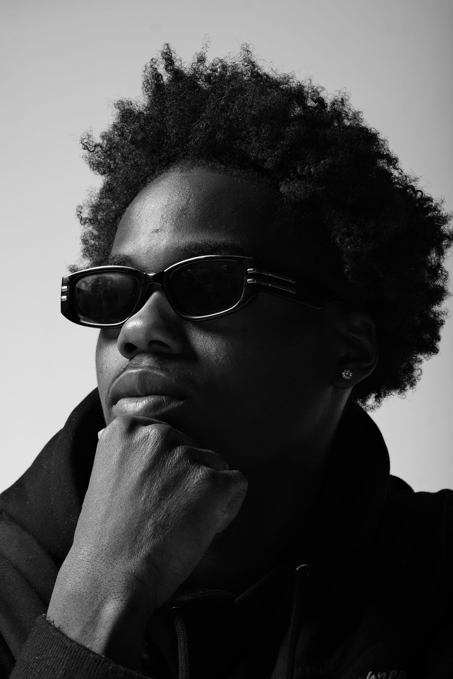 Black and white portrait with sunglasses and natural hair in thoughtful pose.