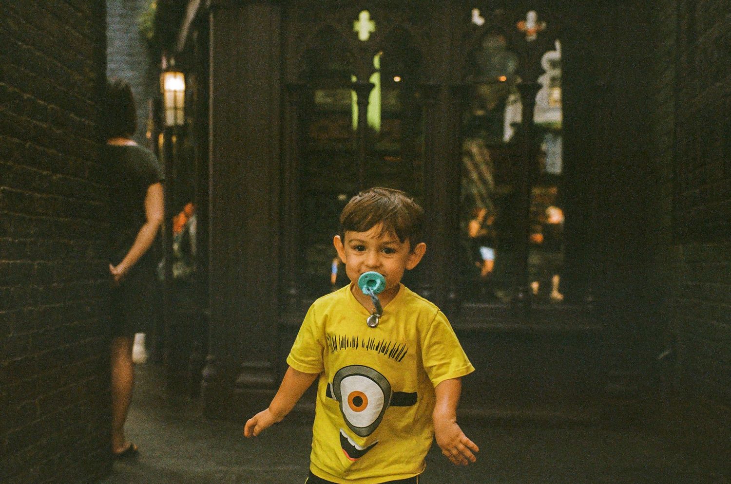 Child in yellow shirt running through dark archway with soft lighting.