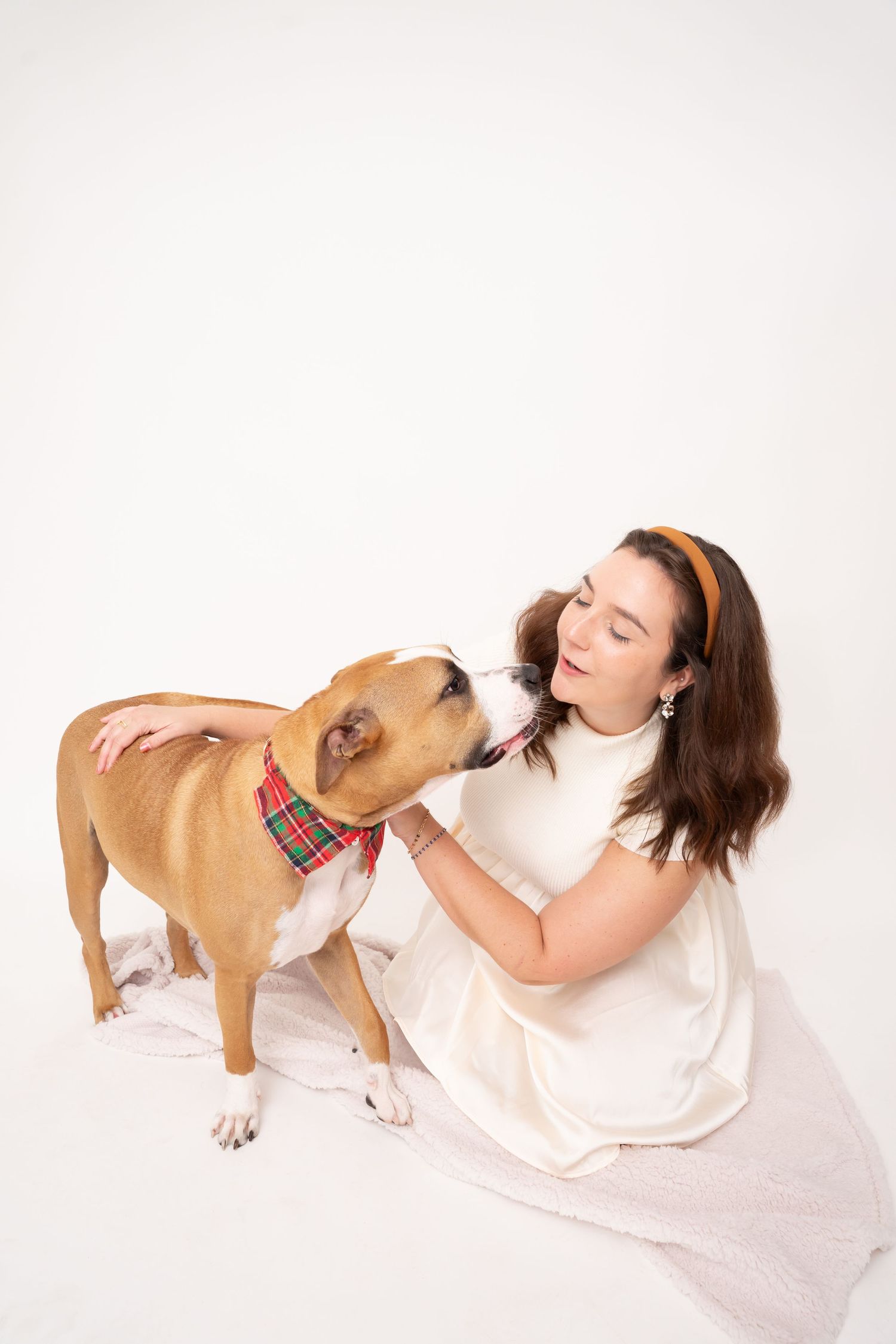 A playful brown dog giving kisses to someone in white against a light background.
