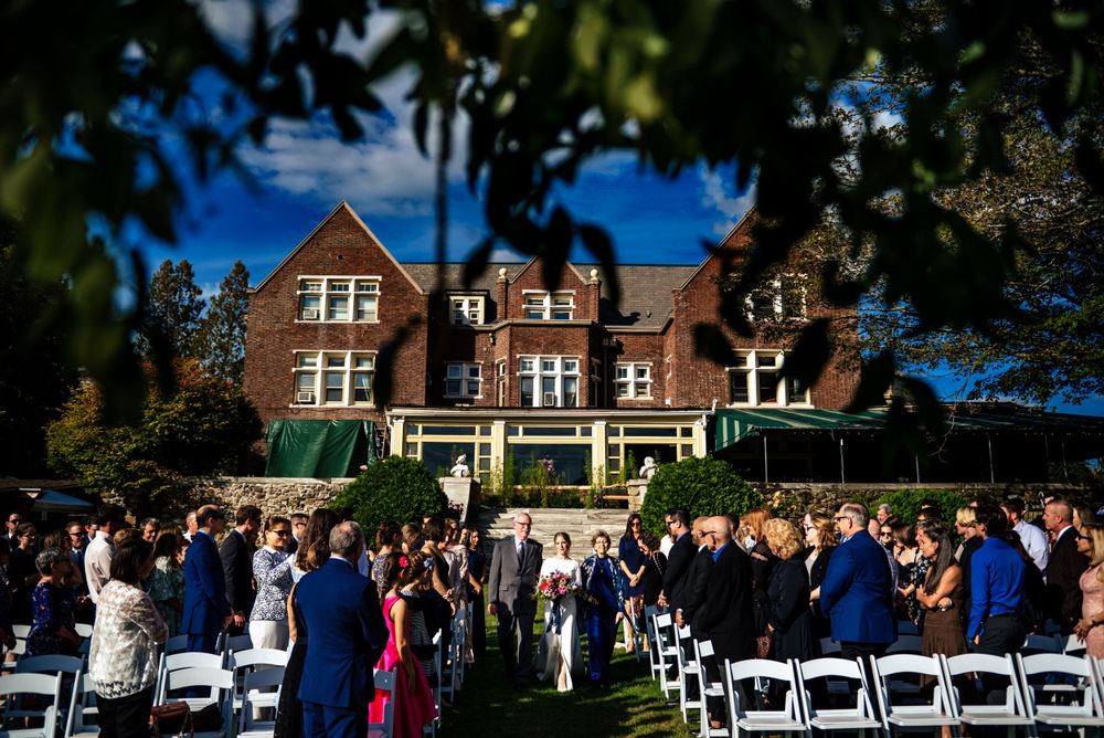 Elegant outdoor wedding ceremony on manicured lawn before grand historic brick manor house.