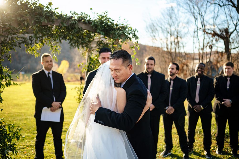 Emotional father hugs bride at altar during outdoor wedding with groomsmen standing nearby.