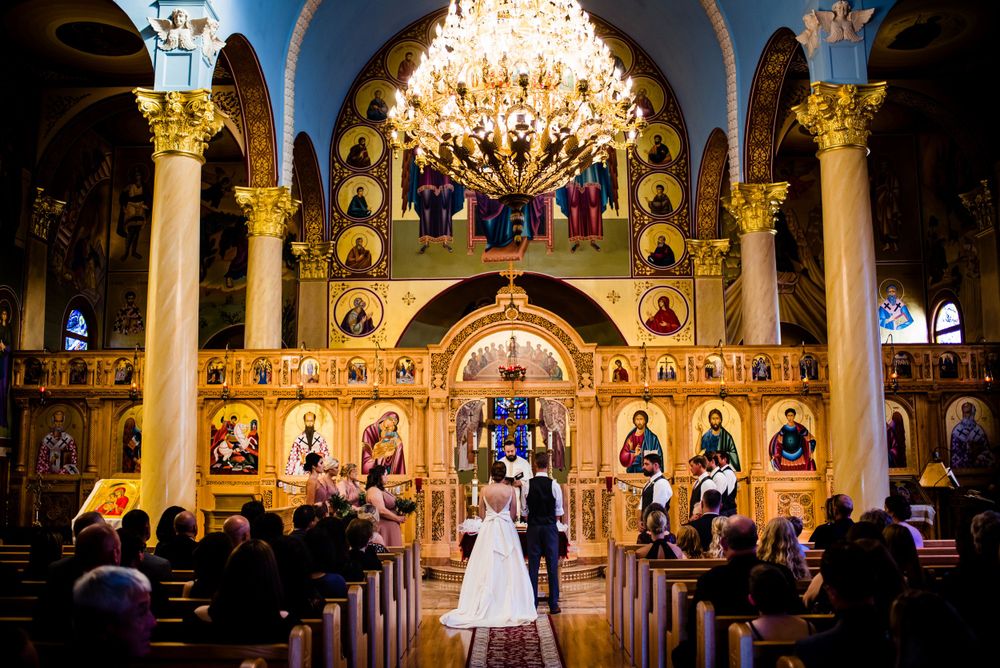Bride and groom stand at ornate golden altar inside stunning Byzantine Orthodox wedding ceremony.