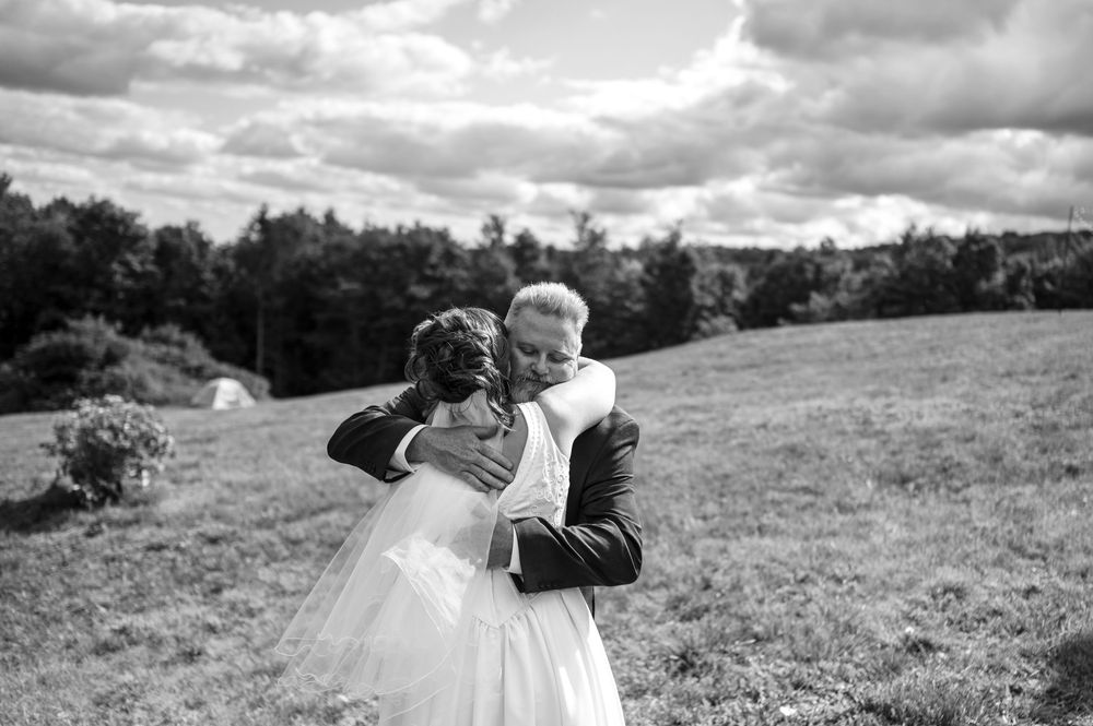 Black and white photo of a bride and groom embracing in a field on their wedding day.