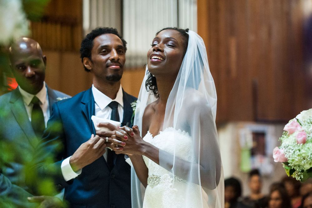 Joyful bride in veil laughs with groom during church wedding ring exchange ceremony.