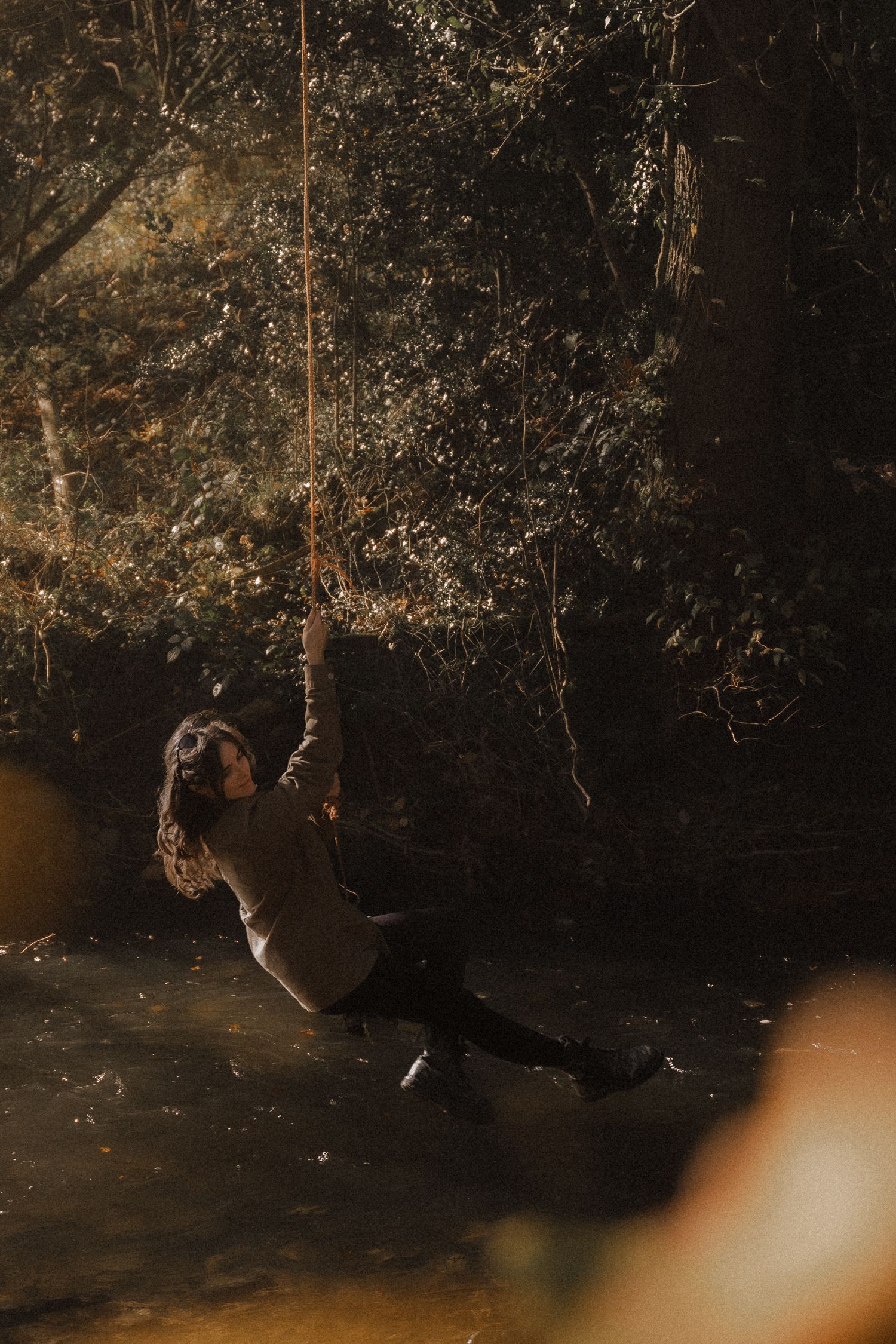 Candid documentary adventure photograph of girl on rope swing over river warm natural lighting
