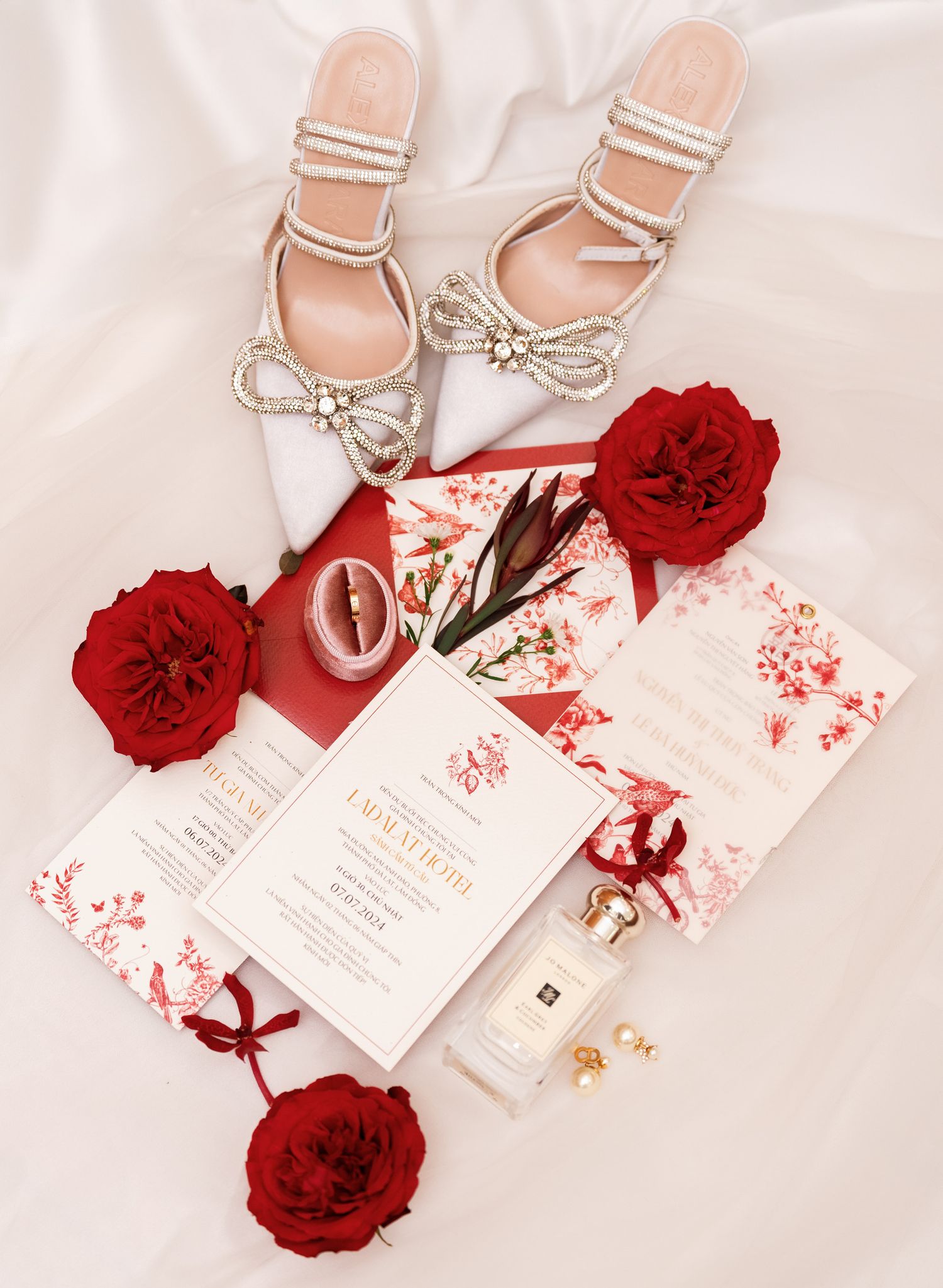 Elegant bridal accessories flatlay with white shoes, red roses and wedding stationery.