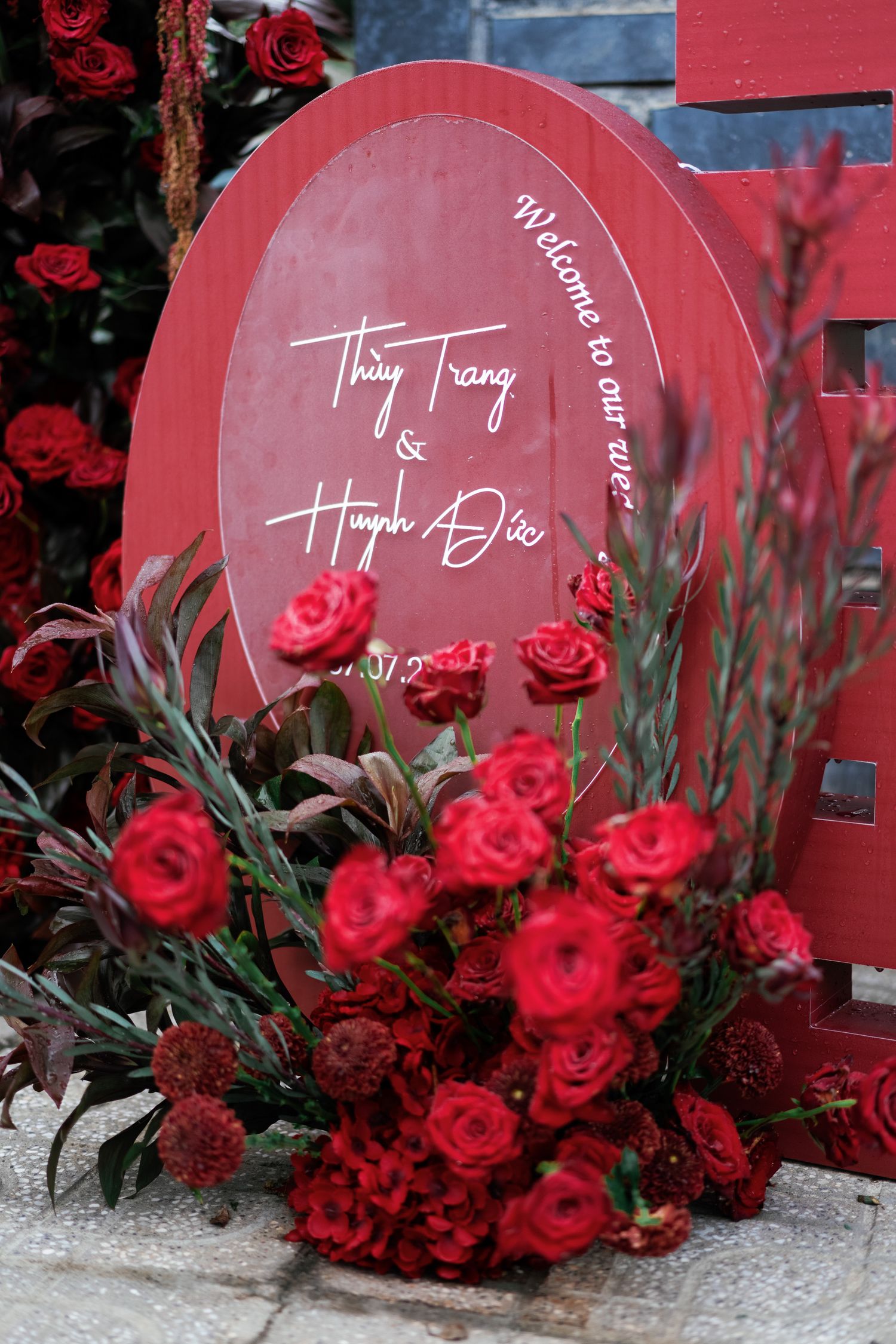 Round red signage with names displayed among vibrant red roses and decorative floral arrangements.