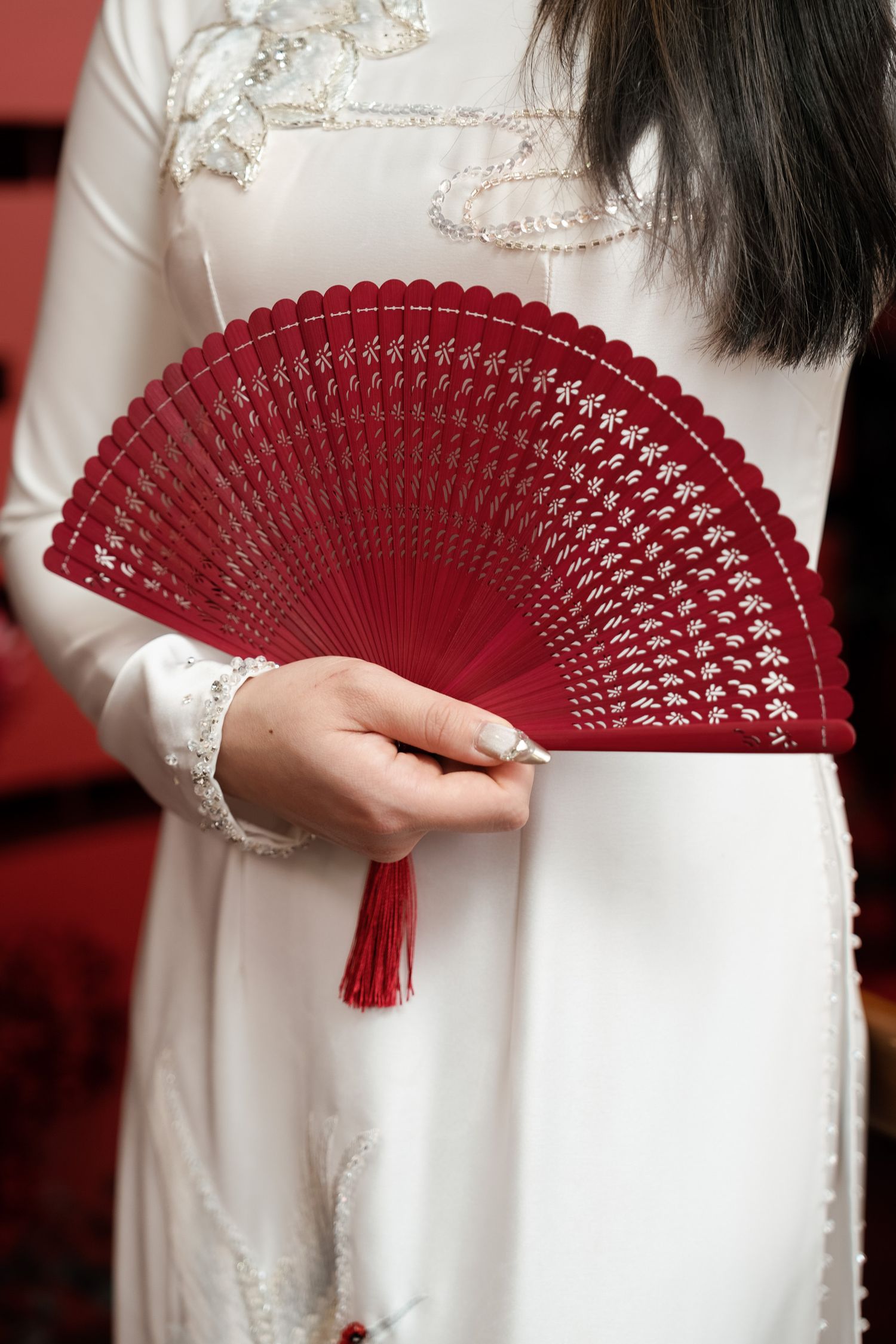 Elegant red folding fan held against white traditional Asian formal attire with embroidery.