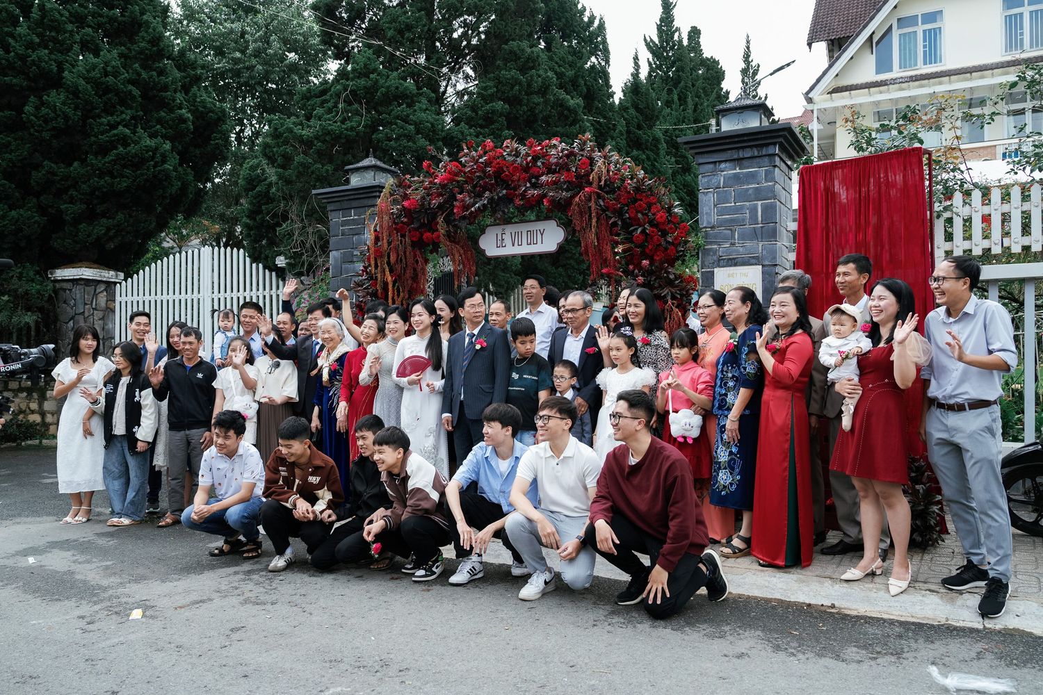Large group photo of wedding guests gathered under floral arch entrance.